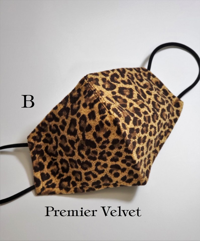 May include: A brown and black leopard print face mask with black elastic ear loops. The mask is made of velvet and has the text "Premier Velvet" printed on the bottom.
