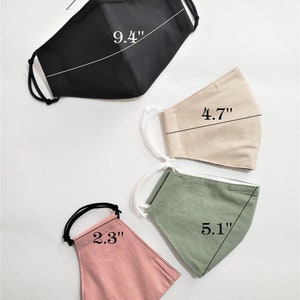 May include: Four fabric face masks in different colors and sizes. The masks are laid out flat on a white surface. The black mask measures 9.4 inches, the beige mask measures 4.7 inches, the green mask measures 5.1 inches, and the pink mask measures 2.3 inches.