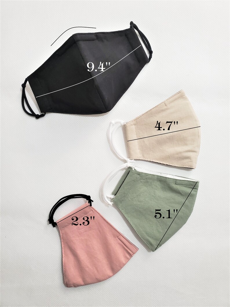 May include: Four fabric face masks in different colors and sizes. The masks are laid out flat on a white surface. The black mask measures 9.4 inches, the beige mask measures 4.7 inches, the green mask measures 5.1 inches, and the pink mask measures 2.3 inches.