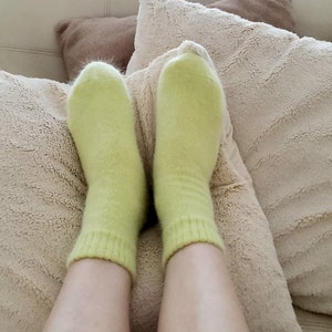 May include: A pair of light lime green ankle socks with a soft, fuzzy texture and a ribbed cuff design. The socks are worn on the feet, covering the ankles and extending slightly upward, featuring a solid color and a knit construction.