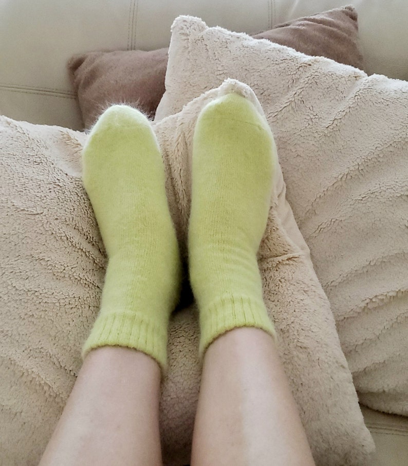 May include: A pair of light lime green ankle socks with a soft, fuzzy texture and a ribbed cuff design. The socks are worn on the feet, covering the ankles and extending slightly upward, featuring a solid color and a knit construction.