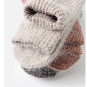 May include: A stack of three pairs of fuzzy, knit socks in neutral tones. The top pair is a light beige, the middle pair is a warm terracotta orange, and the bottom pair is a dark charcoal gray. Each pair features a ribbed cuff and a soft, textured finish.