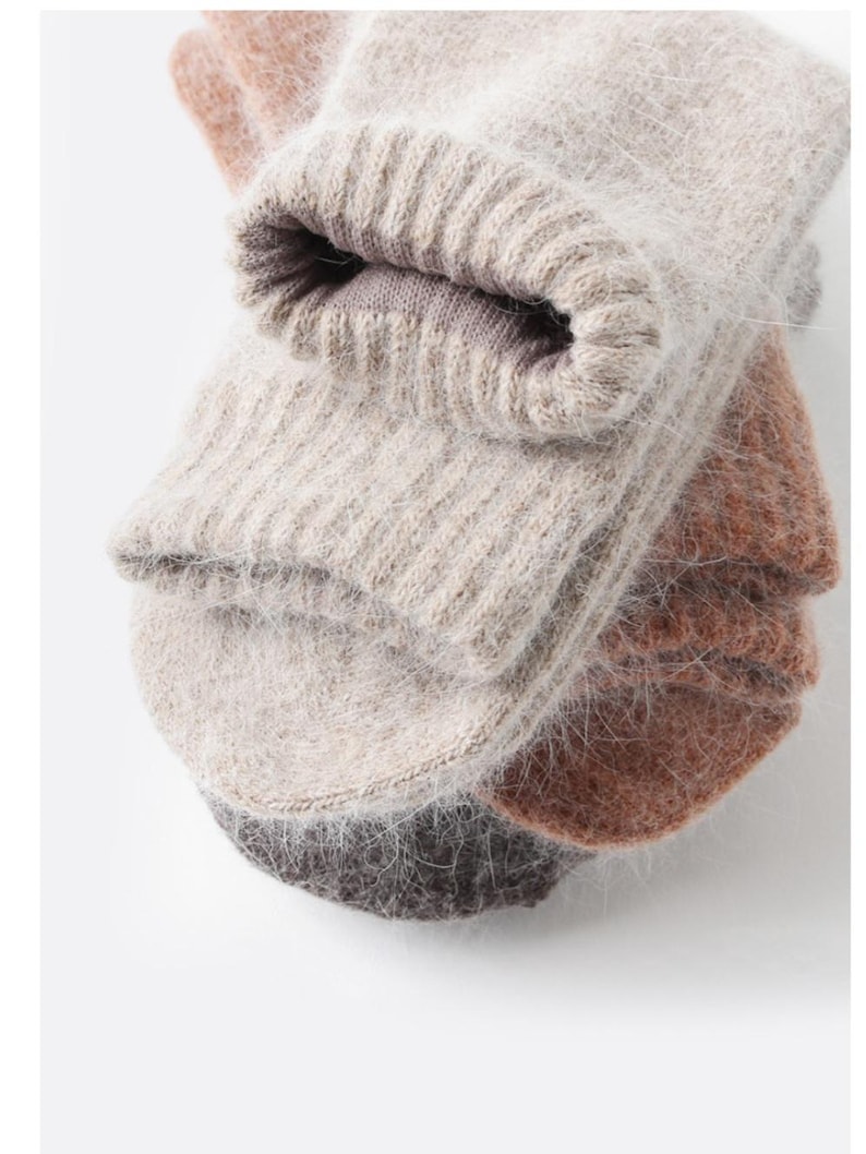 May include: A stack of three pairs of fuzzy, knit socks in neutral tones. The top pair is a light beige, the middle pair is a warm terracotta orange, and the bottom pair is a dark charcoal gray. Each pair features a ribbed cuff and a soft, textured finish.