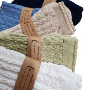 May include: A collection of cable-knit socks in various colors, including light blue, beige, green, white, and navy. Each pair is wrapped with a brown paper band featuring the text "Thank you so much for..." and the website address.