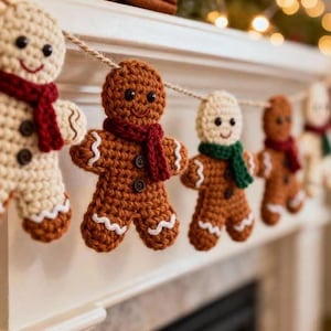 May include: A garland featuring multiple crocheted gingerbread figures strung together on a twine cord. The figures are crafted in light and dark brown yarn, each wearing a small knitted scarf in red or green, with black button eyes and white yarn trim.