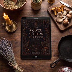 May include: A Samsung tablet displaying a digital meal planner titled The Velvet Cortex Meal Planner, Digital Planner Edition, Planners & Printables for the Divergent Mind, surrounded by a copper bowl, herbs, a candle, mushrooms, and a cast iron pan.