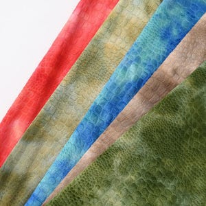 May include: Five strips of fabric arranged diagonally, each featuring a textured, embossed crocodile skin pattern. The colors include vibrant red, muted olive green, bright blue, soft beige, and a deep forest green, all displaying a subtle gradient.