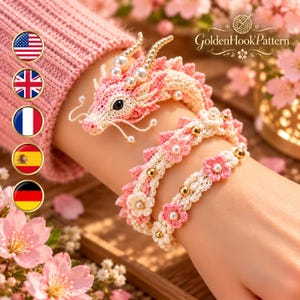 May include: A crochet dragon bracelet in shades of pink and cream, featuring a detailed dragon head with pearl accents, a winding body, and small floral motifs adorned with gold beads and pearls, labeled GoldenHookPattern.