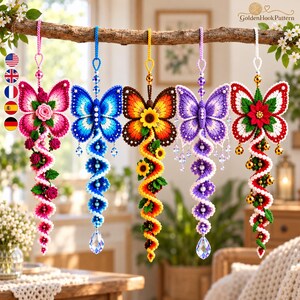 May include: Five hanging crochet butterfly ornaments in pink, blue, yellow, purple, and red-white-green. Each features a central flower, a spiraling tail with small floral or bead accents, and a clear crystal-like teardrop pendant at the bottom.