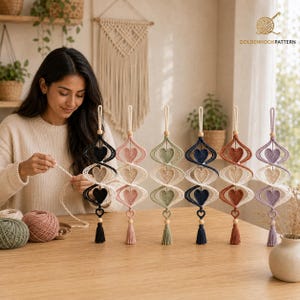 May include: Six vertical macrame wall hangings featuring a spiral design with three crocheted hearts in each. The colors include black, dusty pink, sage green, navy blue, terracotta, and lavender, each finished with a wooden bead and a tassel.