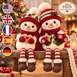 Può includere: Due pupazzi di neve all'uncinetto con corpo bianco, gambe a righe rosse e bianche e stivali marroni. Indossano cappelli rossi con pon pon, sciarpe rosse e gilet verdi. Uno tiene in mano un biscotto a forma di cuore, l'altro un biscotto a stella.