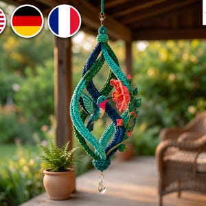 May include: A hanging crochet ornament featuring a spiraling structure in shades of teal and navy blue. A small hummingbird with a pink throat and teal wings is positioned near a bright orange hibiscus flower with green leaves. A clear crystal hangs below.