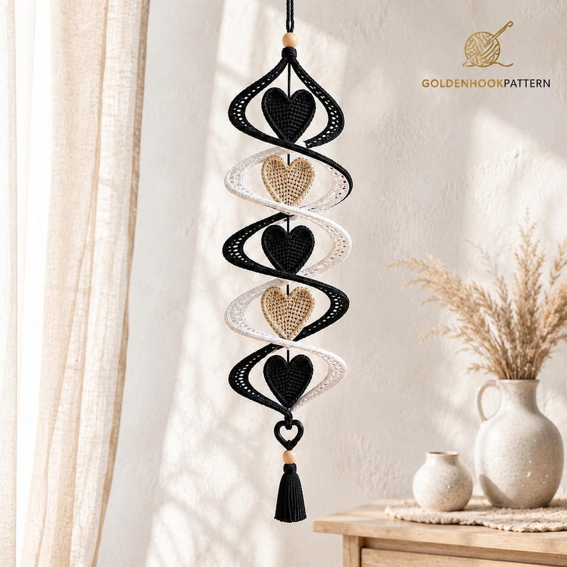 May include: A hanging spiral decoration featuring alternating black and white crocheted ribbons. Five heart-shaped elements are centered within the spiral, alternating between black and beige. The piece includes wooden beads and a black tassel.