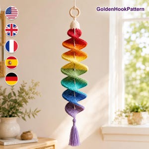 May include: A hanging crochet spiral decoration featuring a vibrant rainbow gradient of red, orange, yellow, green, blue, and purple yarn. The piece is suspended from a wooden ring and finished with a matching purple tassel at the bottom.