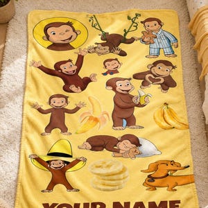 May include: A yellow fleece blanket featuring multiple illustrations of Curious George in various poses, including holding a teddy bear, eating a banana, and wearing a hat. The design includes banana slices and a dachshund, with the text YOUR NAME.