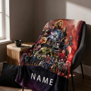 Może przedstawiać: Miękki koc z żywym kolażem superbohaterów Marvela na czerwonym, kosmicznym tle. Dolna część przechodzi w ciemnofioletowy i czarny motyw kosmiczny, z napisem NAME wydrukowanym białymi wielkimi literami na powierzchni materiału.