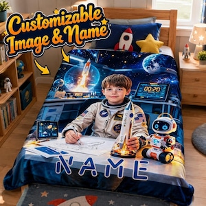 Puede incluir: Una manta personalizable con un gráfico de temática espacial de un niño con traje de astronauta sentado en un escritorio con un modelo de cohete, un robot y pantallas digitales. El texto "Customizable Image & Name" y "NAME" está impreso.