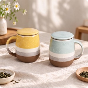 May include: Two ceramic mugs with lids, each featuring a speckled finish and a horizontal colour-blocked design. One mug has yellow, white, grey, and brown bands, while the other has light blue, white, grey, and brown bands, both with handles.