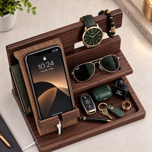 May include: A dark wood desk organizer featuring a smartphone charging stand, a watch holder, a shelf for sunglasses, and a tray for accessories. The organizer holds a smartphone, a green-faced watch, black sunglasses, a car key, a pen, and a ring.
