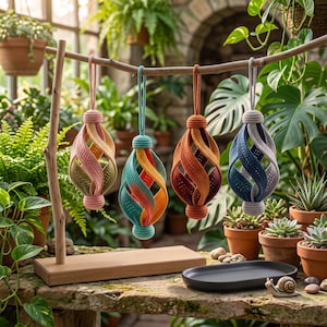 Pode incluir: Quatro ornamentos decorativos suspensos com uma estrutura em espiral tipo gaiola feita de tecido de croch&ecirc;. Cada ornamento apresenta uma combina&ccedil;&atilde;o de cores &uacute;nica, incluindo rosa, azul-petr&oacute;leo, laranja e azul, suspensos num suporte de madeira.