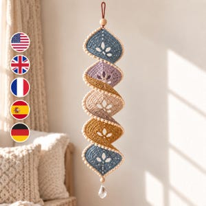 May include: A hanging spiral mobile featuring five crocheted diamond-shaped segments in blue, lavender, beige, and mustard yellow. Each segment has a central cutout, and the structure is accented with small wooden beads and a clear crystal pendant.