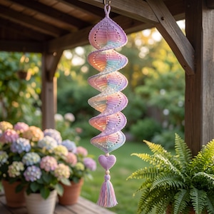 Può includere: Un decoro a spirale realizzato all'uncinetto con una sfumatura di colori pastello rosa, blu e viola. L'oggetto da appendere presenta un piccolo cuore all'uncinetto, perline di legno e una nappa multicolore all'estremità inferiore.