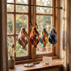 Pode incluir: Quatro ornamentos de croch&ecirc; suspensos com um design de gaiola aberta torcida em paletas de cores rosa pastel, laranja, azul-petr&oacute;leo e azul. Cada ornamento possui uma al&ccedil;a para pendurar. Uma placa na superf&iacute;cie de madeira diz HANDMADE CROCHETED TWISTS.