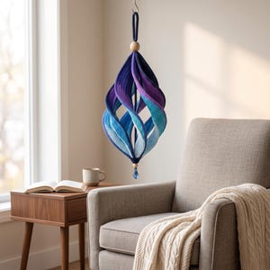 May include: A hanging spiral ornament featuring a gradient of colors transitioning from deep navy blue to vibrant purple, teal, and light blue. The structure is suspended by a cord with a wooden bead at the top and a small blue crystal at the bottom.