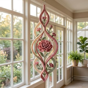 May include: A hanging wall decoration featuring a vertical, twisted frame made of crocheted yarn in shades of cream, sage green, and dusty rose. The structure is adorned with crocheted flowers and leaves, including a large central rose bloom.