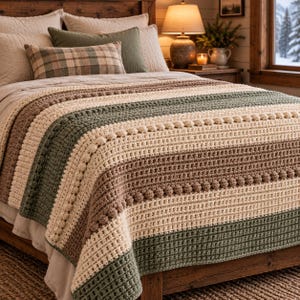 May include: A crocheted throw blanket featuring horizontal stripes in shades of cream, sage green, and tan. The blanket incorporates textured bobble stitch rows interspersed with solid double crochet sections, creating a layered, tactile surface.