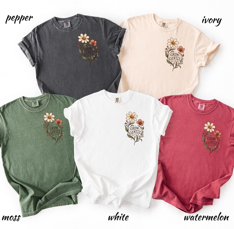 May include: Five short-sleeved crew neck t-shirts in pepper, ivory, moss, white, and watermelon colours. Each shirt features a small floral graphic on the left chest with the text "GROW GENTLY" printed in a script font amidst brown and white flowers.