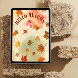 以下が含まれることがあります： 「HELLO AUTUMN」という茶色の文字が書かれたデジタルグラフィックを表示するタブレット。クリーム色と薄緑色の背景に、オレンジ、赤、黄色の水彩画風のモミジの葉が散りばめられています。