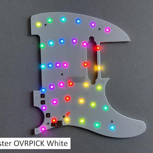 May include: A white Telecaster guitar pickguard featuring an integrated array of multicolored LED lights. The surface includes cutouts for pickups and controls, with the text Telecaster OVRPICK White printed at the bottom left corner.