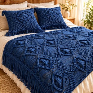 May include: Two square throw pillows and a large rectangular throw blanket in deep navy blue. Each piece features intricate macrame knotting with a repeating diamond pattern and long, decorative fringe along the edges, layered over a white bed.