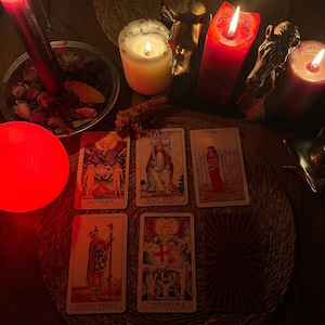 Pode incluir: Uma tiragem de seis cartas de tarot, incluindo Os Amantes, Rei de Espadas, Oito de Espadas, Pajem de Paus e O Julgamento, dispostas sobre um tapete tran&ccedil;ado com velas acesas, uma tigela de metal com p&eacute;talas secas e figuras douradas.