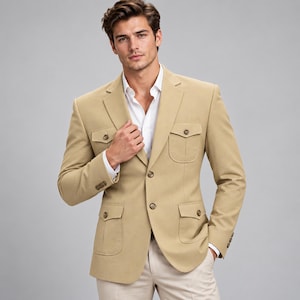 Op de afbeelding: Een beige safari-stijl blazer met een ingekeepte revers, twee borstzakken met knopen en twee heupzakken met knopen. Het jasje wordt gedragen over een wit overhemd met kraag, met drie knopen op elke mouw en een sluiting met twee knopen.
