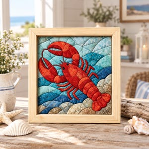 May include: A square framed fabric wall art piece featuring a quilted lobster in vibrant red tones. The lobster is centred against a background of layered, wavy fabric patches in shades of light blue, deep blue, and sandy beige, creating a textured ocean scene.