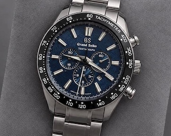 May include: A Grand Seiko Tentagraph chronograph watch with a textured blue dial, silver-tone hands and indices, and a black ceramic tachymeter bezel. The timepiece features a stainless steel link bracelet and a date display window.