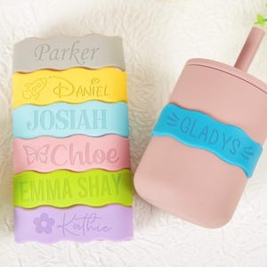 Pu&ograve; includere: Una pila di sei fasce in silicone colorate con bordi ondulati, ognuna incisa con un nome e un'icona unici, tra cui Parker, Daniel con un razzo, Josiah, Chloe con una farfalla, Emma Shay e Kathie con un fiore, pi&ugrave; una tazza rosa con cannuccia.