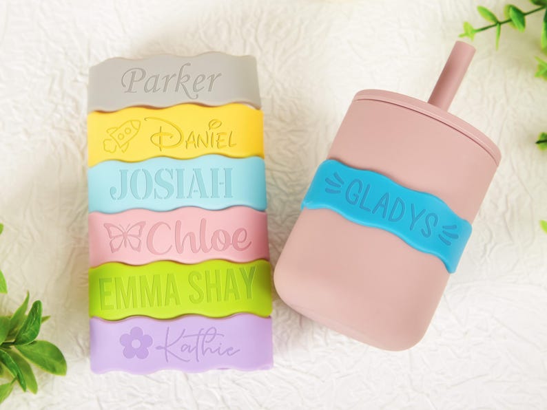 Pu&ograve; includere: Una pila di sei fasce in silicone colorate con bordi ondulati, ognuna incisa con un nome e un'icona unici, tra cui Parker, Daniel con un razzo, Josiah, Chloe con una farfalla, Emma Shay e Kathie con un fiore, pi&ugrave; una tazza rosa con cannuccia.