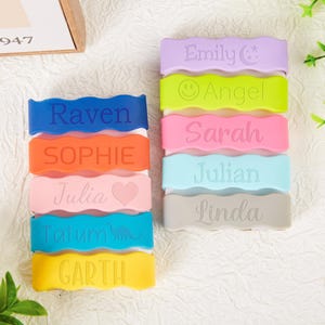 Pu&ograve; includere: Una collezione di dieci fasce in silicone con bordi ondulati, ognuna personalizzata con un nome e un'icona unici. Le fasce sono disponibili nei colori viola, verde lime, rosa, azzurro, grigio, blu scuro, arancione, rosa chiaro, turchese e giallo.