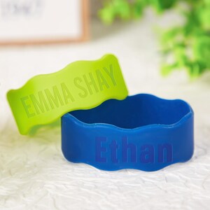 Pu&ograve; includere: Due braccialetti in silicone con bordi ondulati. Un braccialetto &egrave; verde lime con il nome EMMA SHAY in rilievo in lettere maiuscole. L'altro braccialetto &egrave; blu reale con il nome Ethan in rilievo in un mix di lettere maiuscole e minuscole.