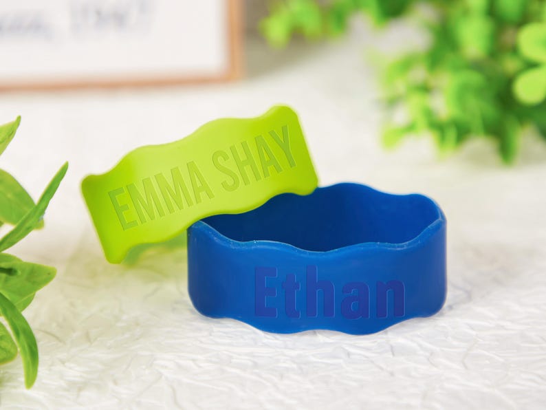 Pu&ograve; includere: Due braccialetti in silicone con bordi ondulati. Un braccialetto &egrave; verde lime con il nome EMMA SHAY in rilievo in lettere maiuscole. L'altro braccialetto &egrave; blu reale con il nome Ethan in rilievo in un mix di lettere maiuscole e minuscole.