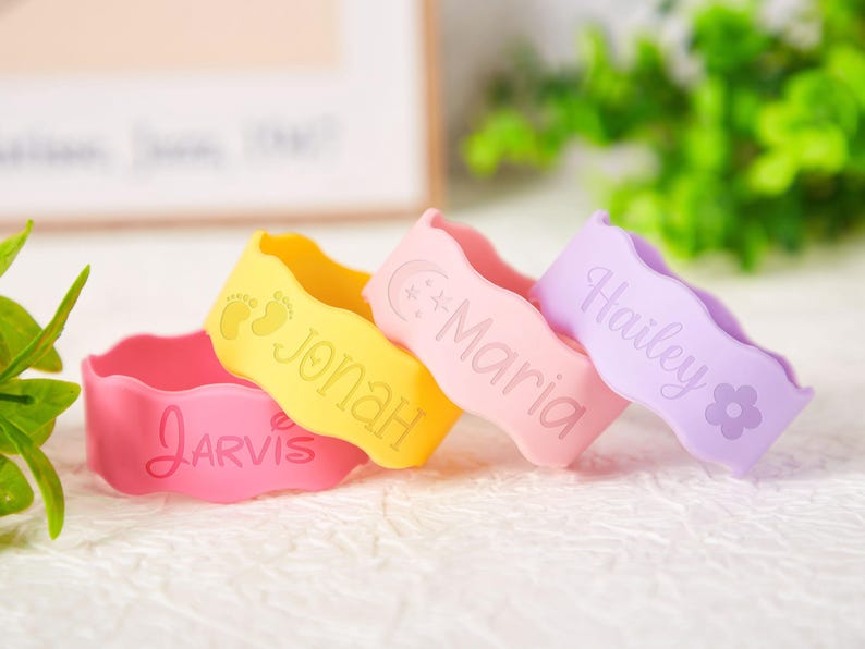 Pu&ograve; includere: Quattro braccialetti ondulati in silicone nei colori rosa, giallo, rosa chiaro e lavanda. Il braccialetto rosa riporta il nome Jarvis. Quello giallo mostra impronte di piedi di neonato e il nome Jonah. Il rosa chiaro presenta una luna, stelle e il nome Maria. Il braccialetto lavanda mostra il nome Hailey e un'icona a forma di fiore.
