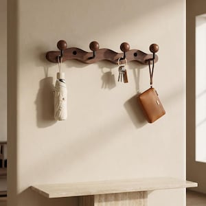 May include: A wall-mounted coat rack featuring a wavy dark wood base with four black metal hooks topped with round wooden knobs. The rack holds a beige umbrella, a set of silver keys on a ring, and a small brown leather pouch with a wrist strap.