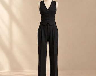 Può includere: Un completo composto da gilet e pantaloni a vita alta gessati neri su un manichino. Il gilet presenta uno scollo a V con quattro bottoni, mentre i pantaloni hanno un davanti plissettato e un taglio a gamba dritta con motivo verticale.