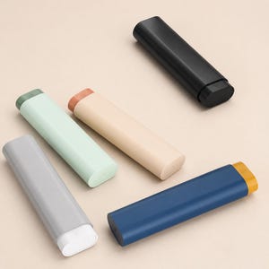 May include: Five elongated, oval-shaped storage cases in various colors: black, beige with a peach cap, light green with a dark green cap, gray with a white cap, and dark blue with a mustard yellow cap. Each case features a smooth, matte finish.