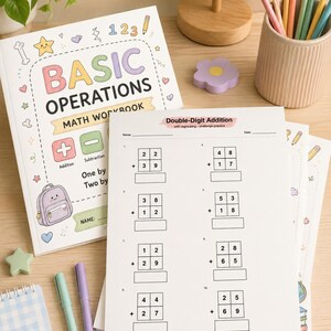 K&ouml;nnte beinhalten: Ein Mathematik-Arbeitsheft mit dem Titel Basic Operations mit pastellfarbenen Illustrationen von Rucksack, Sternen und Herzen, neben einem Arbeitsblatt f&uuml;r zweistellige Addition, Buntstiften im Becher und zwei Stiften auf einer Holzoberfl&auml;che.