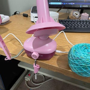 Może przedstawiać: Różowy elektryczny nawijacz do włóczki z białym kablem i turkusową kulką włóczki na drewnianym stole.