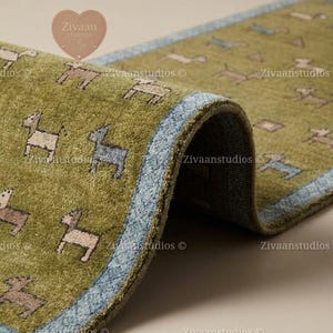 Könnte beinhalten: Ein rechteckiger Teppich mit olivgrünem Grund und einem sich wiederholenden Muster aus kleinen, stilisierten Tierfiguren in Hellbraun und Blau. Der Teppich hat einen strukturierten Flor und einen markanten hellblauen Rand an den Stoffkanten.